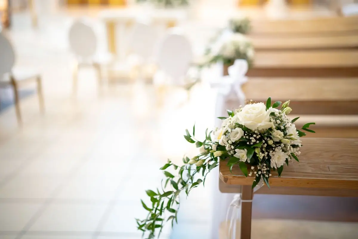 Pale roses and greenery tied to a bench at the end of an aisle