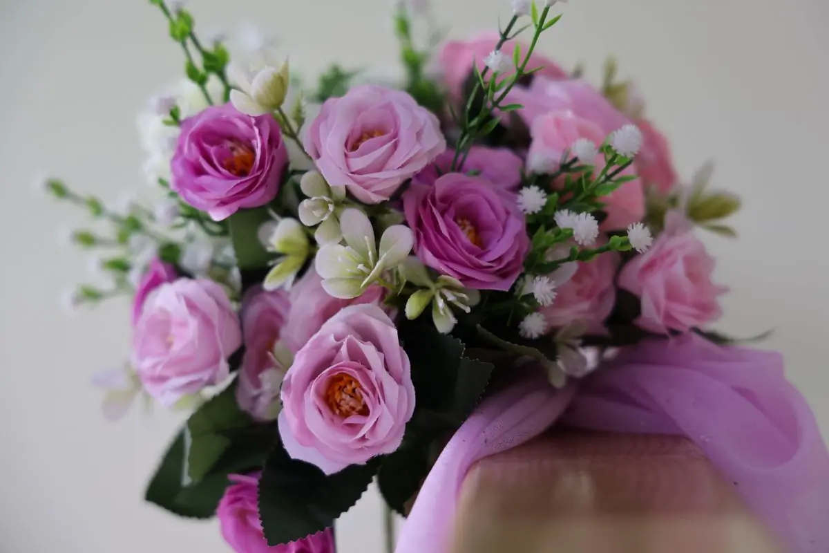 A hand-tied bouquet of pink garden roses against a pale wall