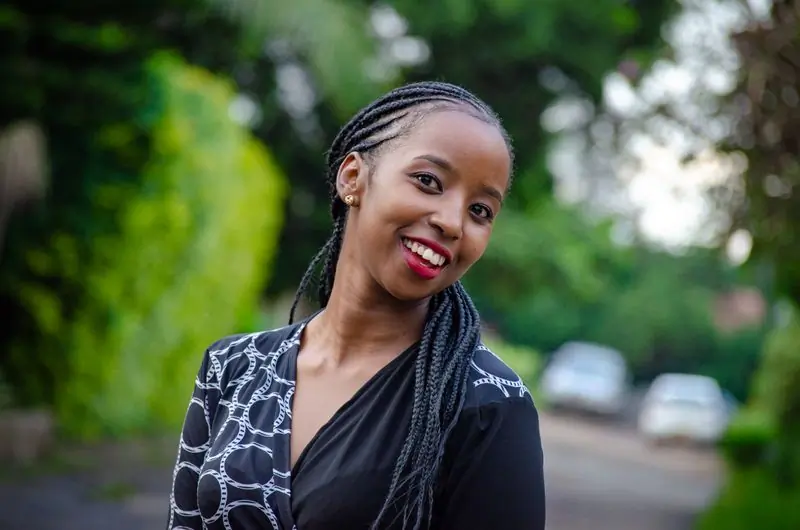A studio manager with braided hair, smiling on a tree-lined road