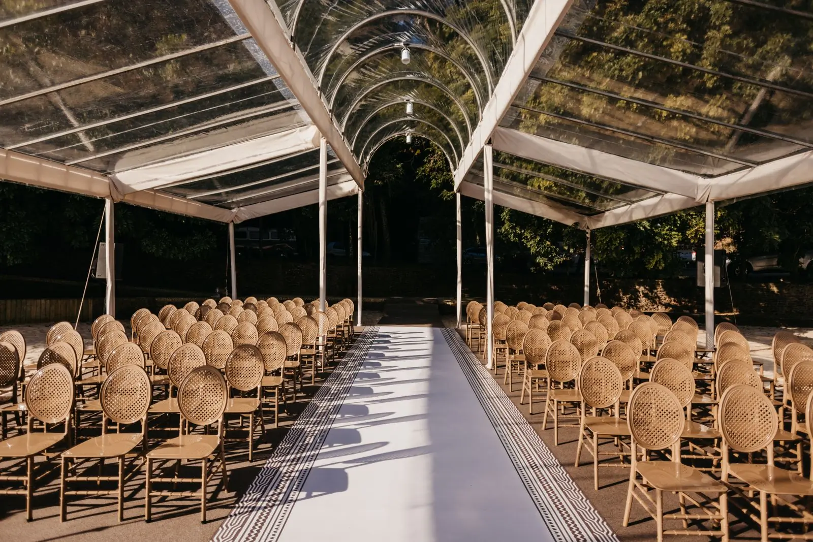 A long aisle of woven chairs under a clear-roofed structure, set and empty