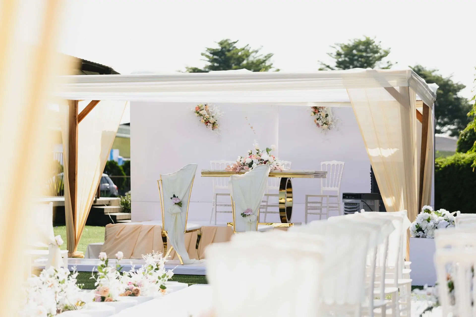 A white and pastel ceremony setting with draped fabric and floral arrangements
