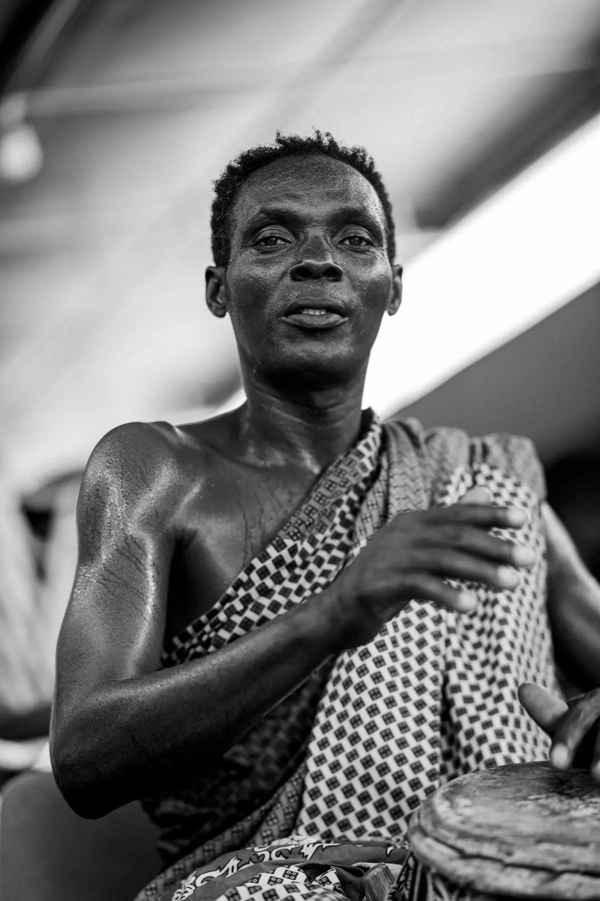 A drummer of a Ghanaian kete ensemble mid-stroke, photographed in black and white