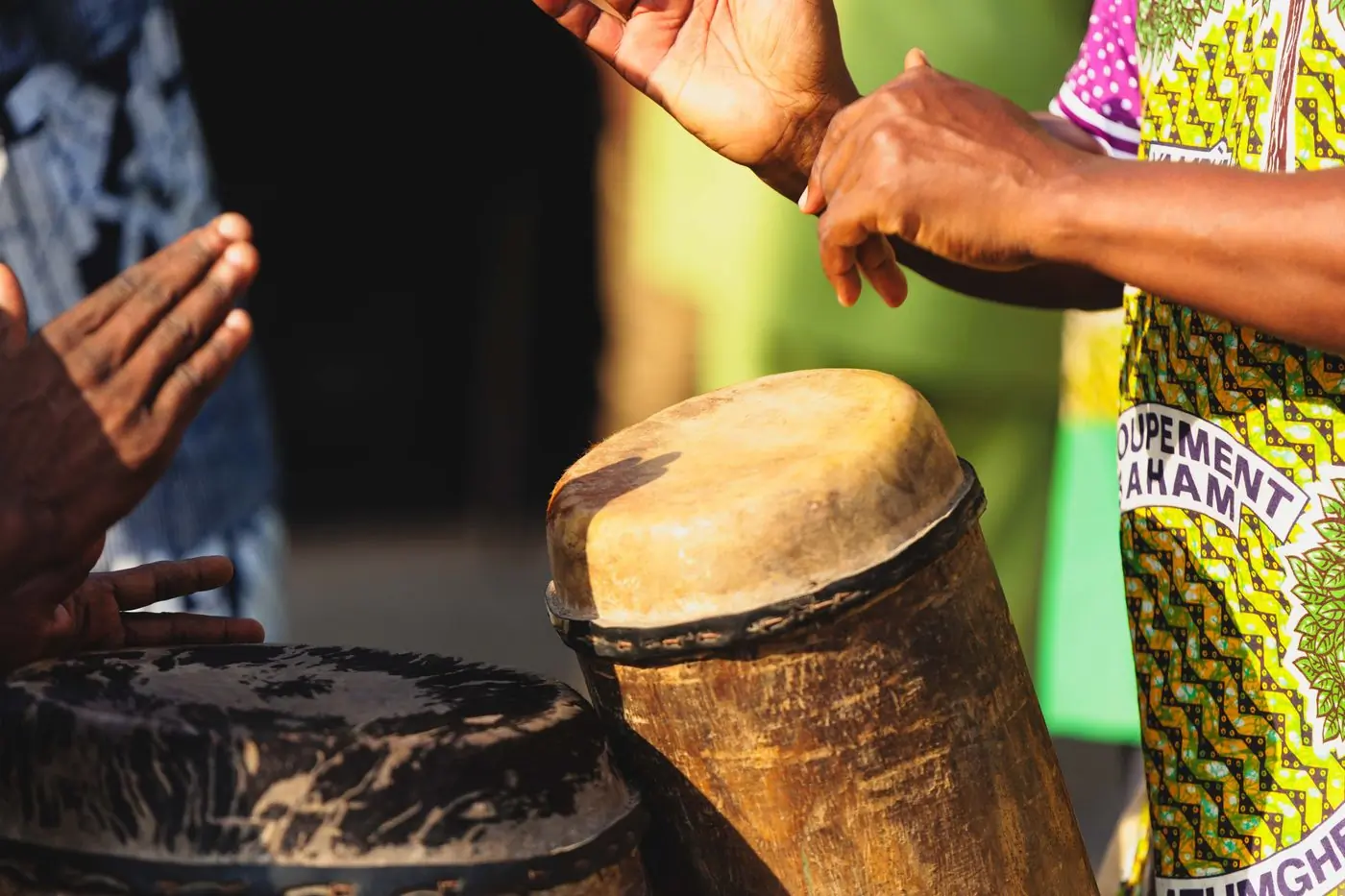 Hands playing traditional drums against a painted green wall
