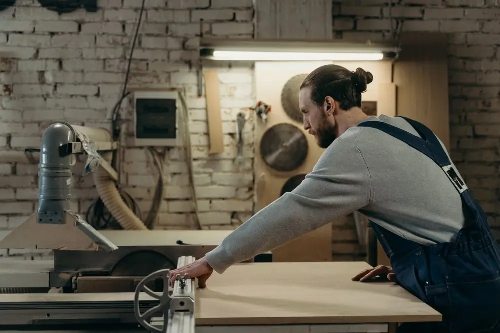 A joiner running a board through a sliding table saw