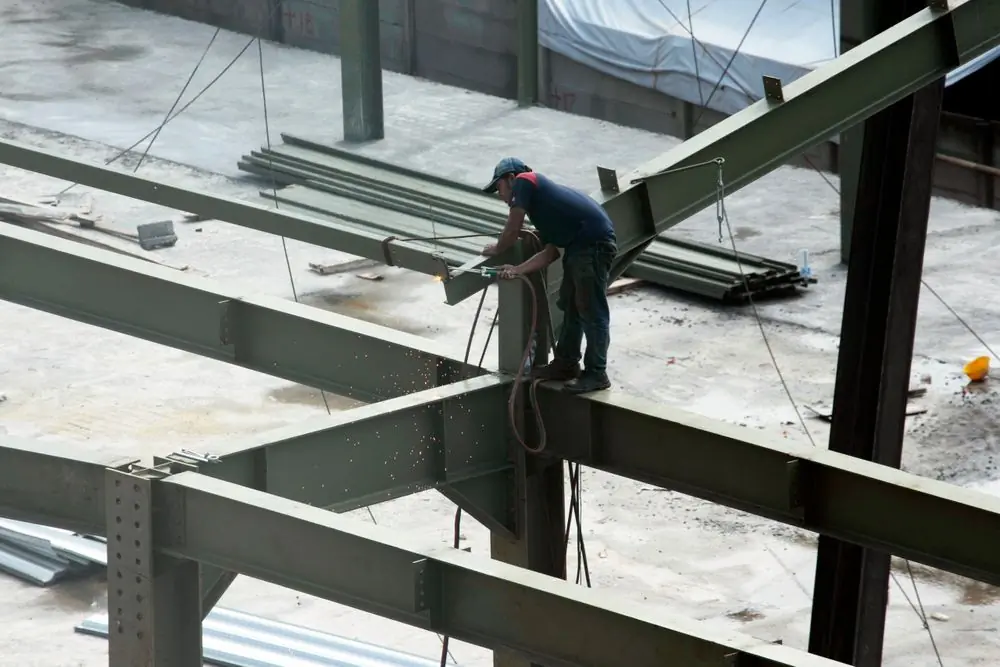 A welder joining steel beams high on a frame