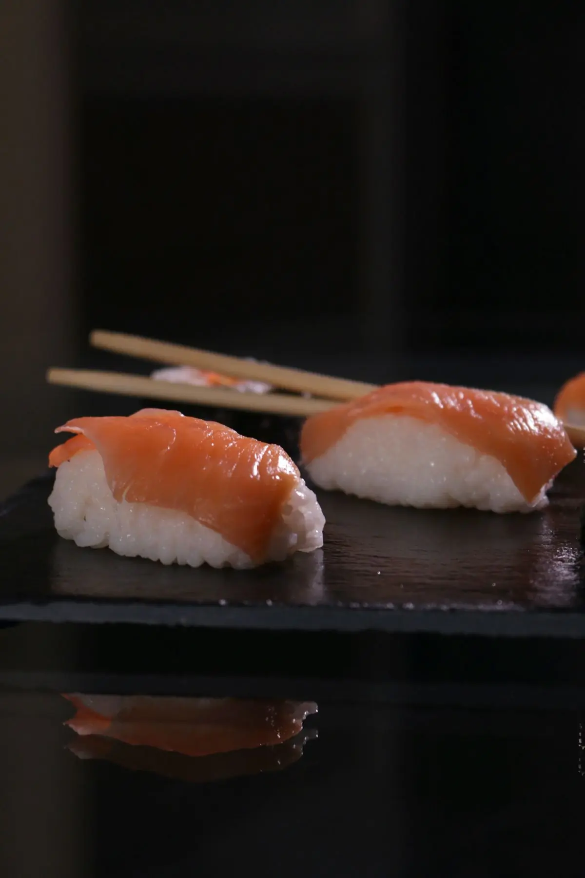 Two pieces of salmon nigiri on a dark surface