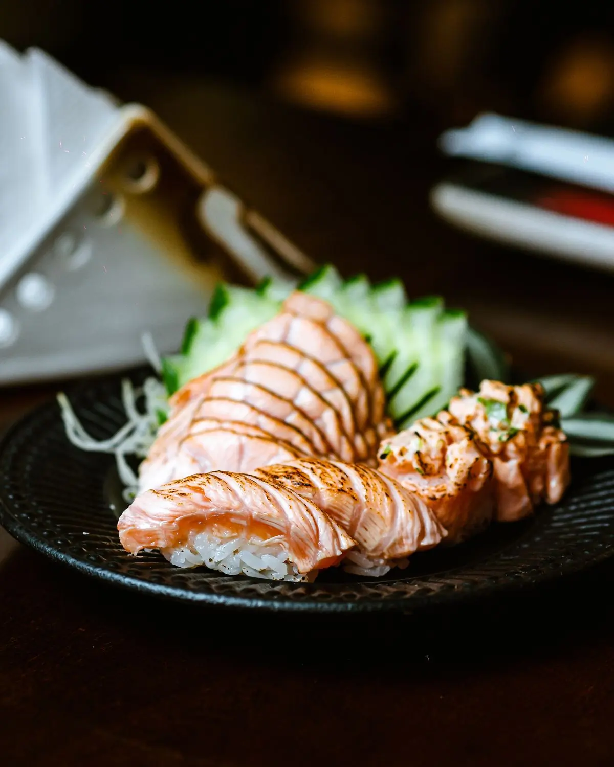 Salmon nigiri plated on dark ceramic