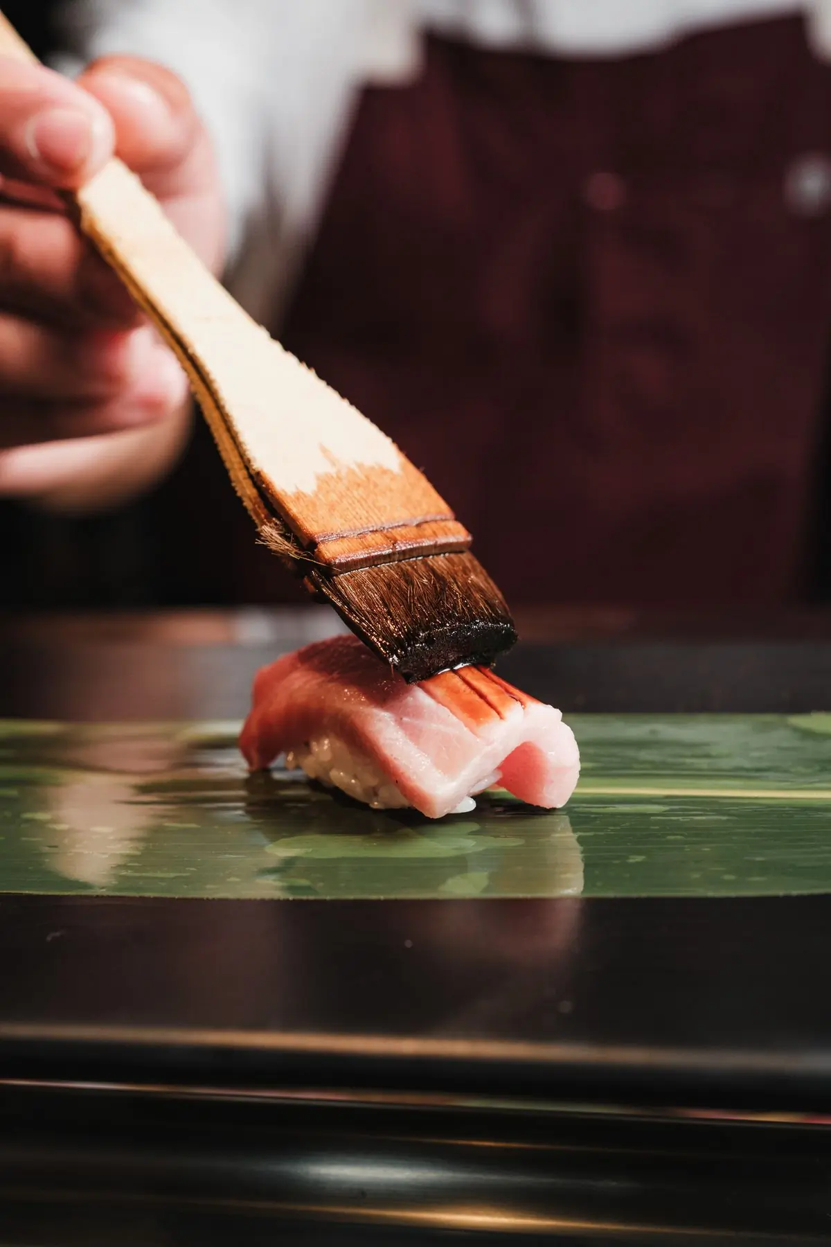 A brush glazing a piece of nigiri