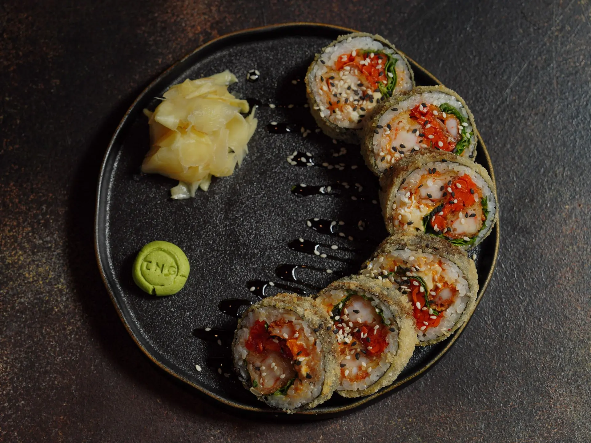 Maki rolls arranged around a dark ceramic plate with wasabi and ginger