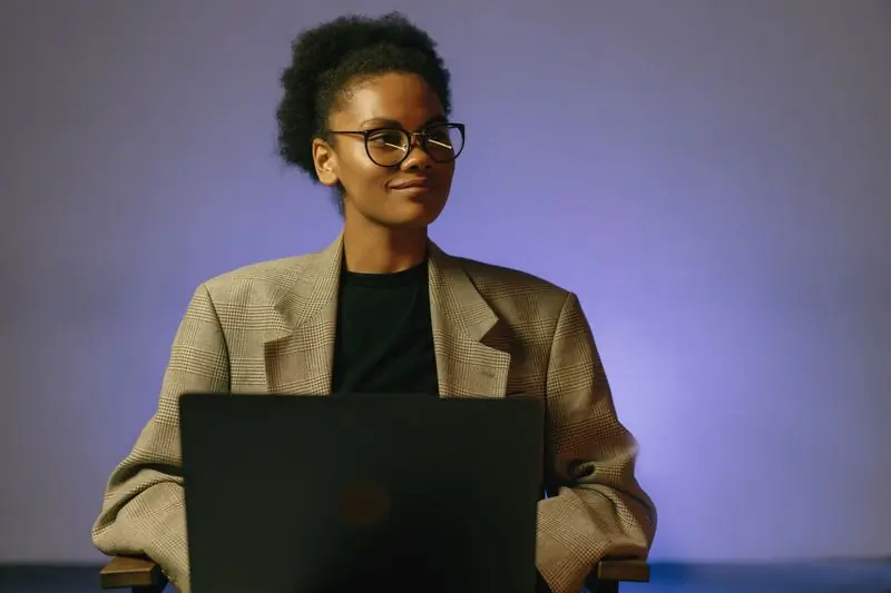 A person in a tan blazer working at a laptop against a violet backdrop