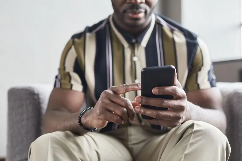 A man in a striped shirt sitting down with a phone in one hand