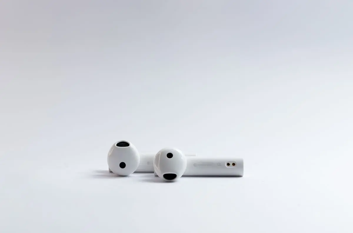 A pair of white wireless earbuds beside their case on white