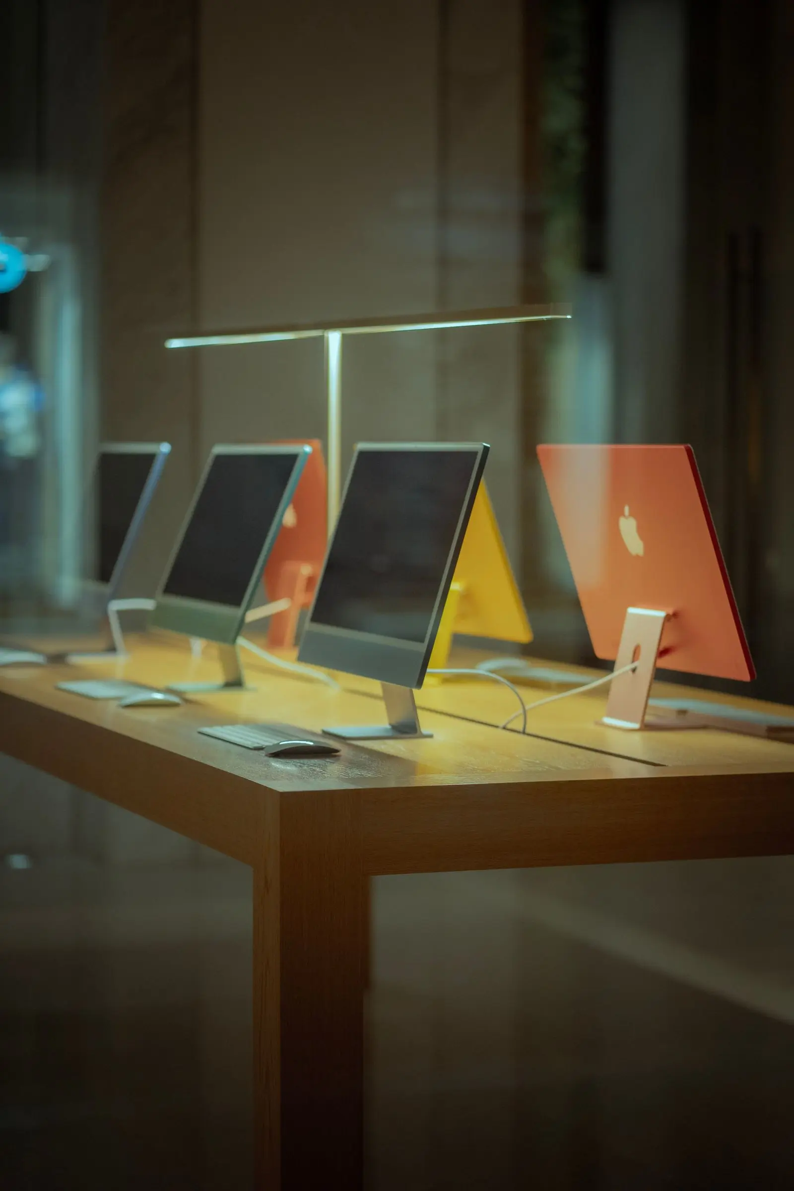 A row of desktop computers on a wooden display table in a shop