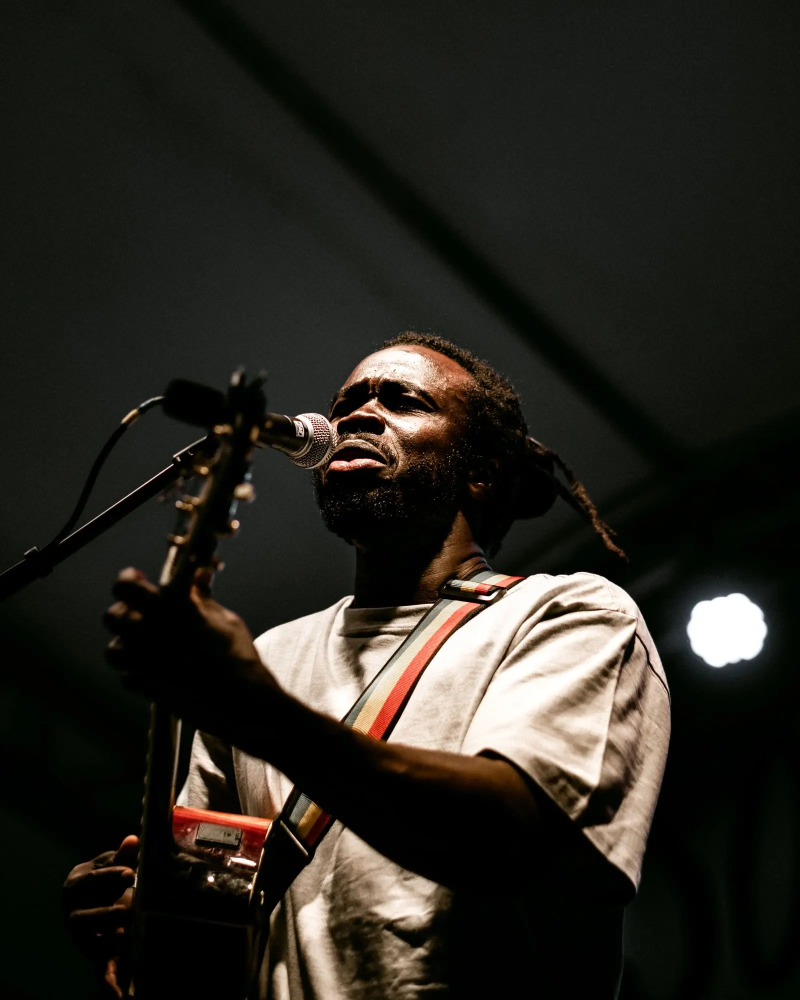 A singer with locs playing an acoustic guitar into a stage microphone