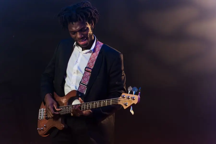 Kwabena Asare playing electric bass under a warm stage light