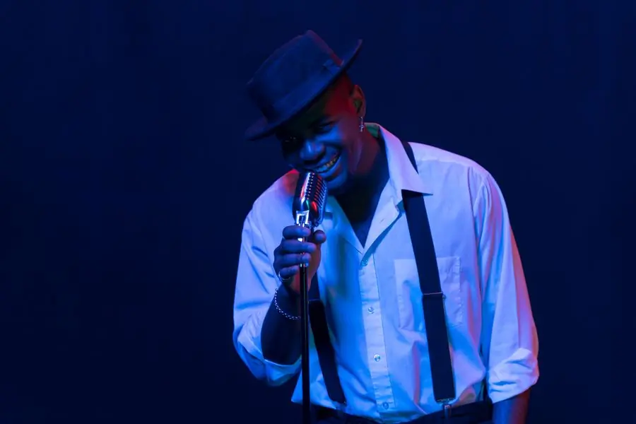 Nii Lartey in a hat singing into a microphone under blue light