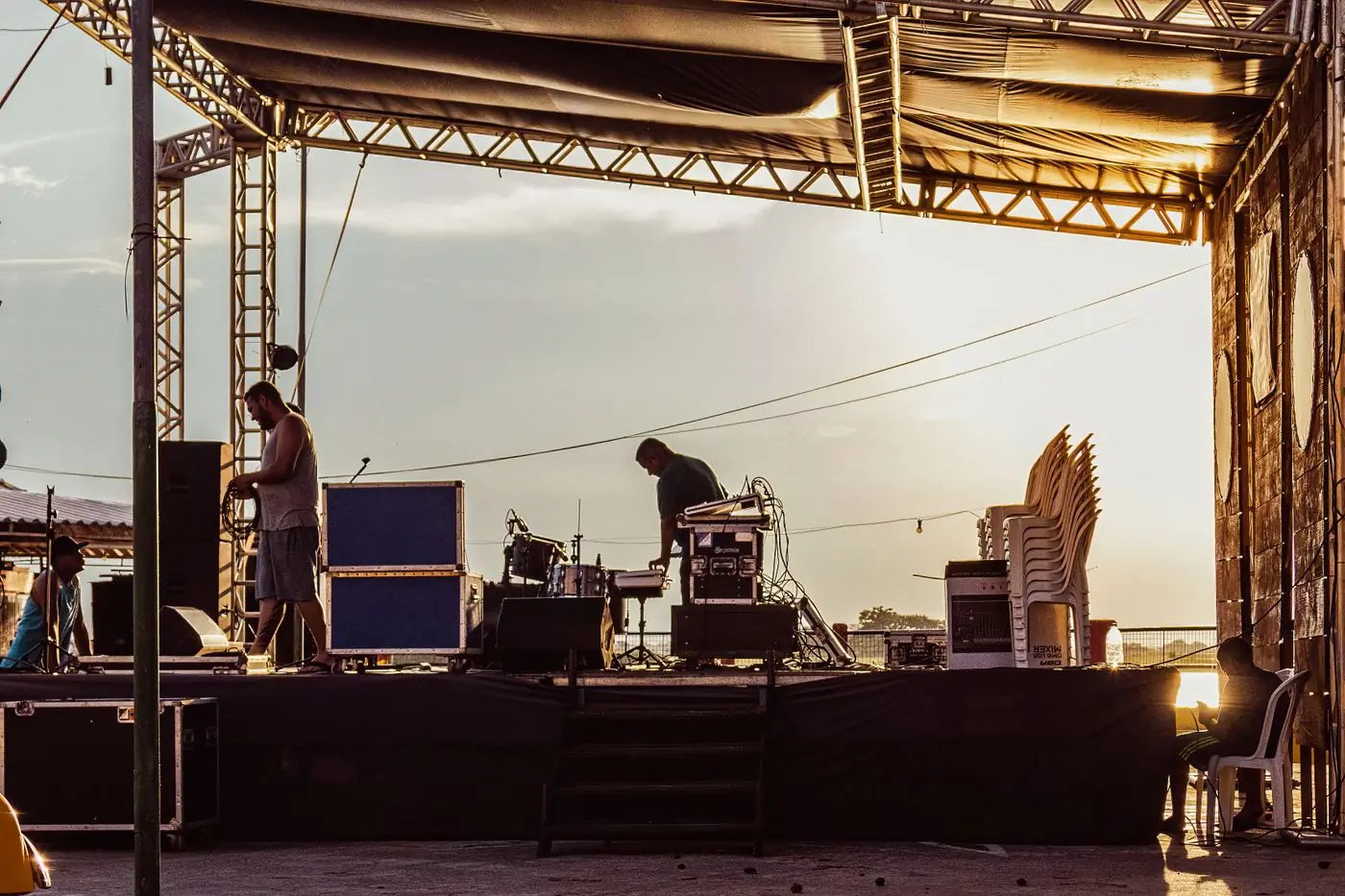 A crew building an outdoor stage as the sun sets behind it