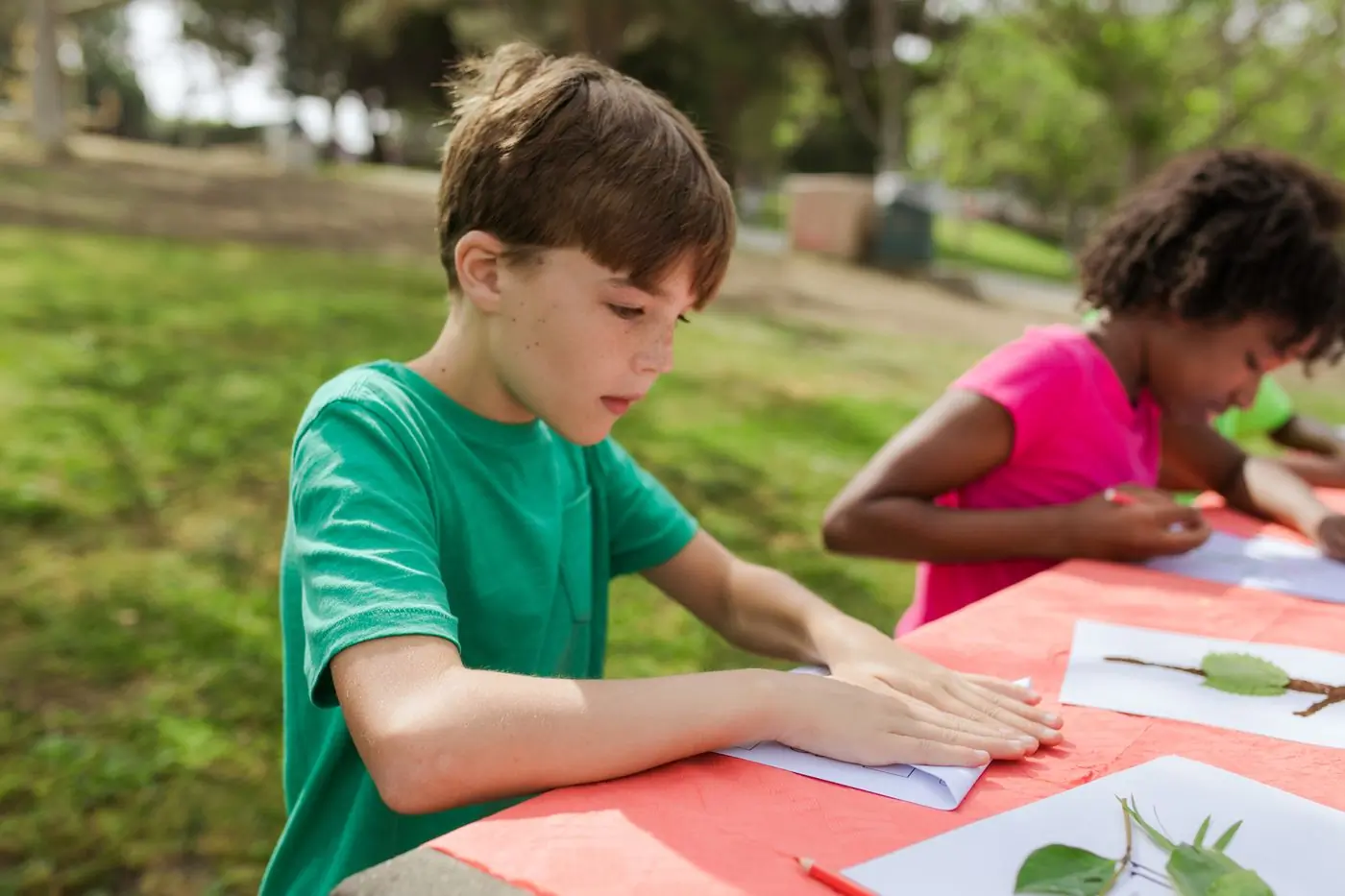 A camper working on a craft project at a long table outdoors