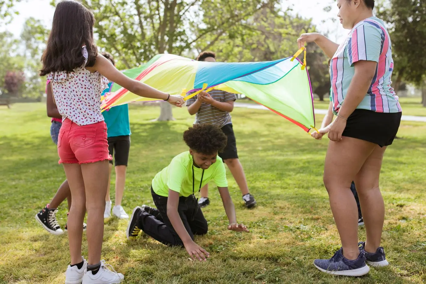 Campers holding the edges of a coloured parachute on the grass