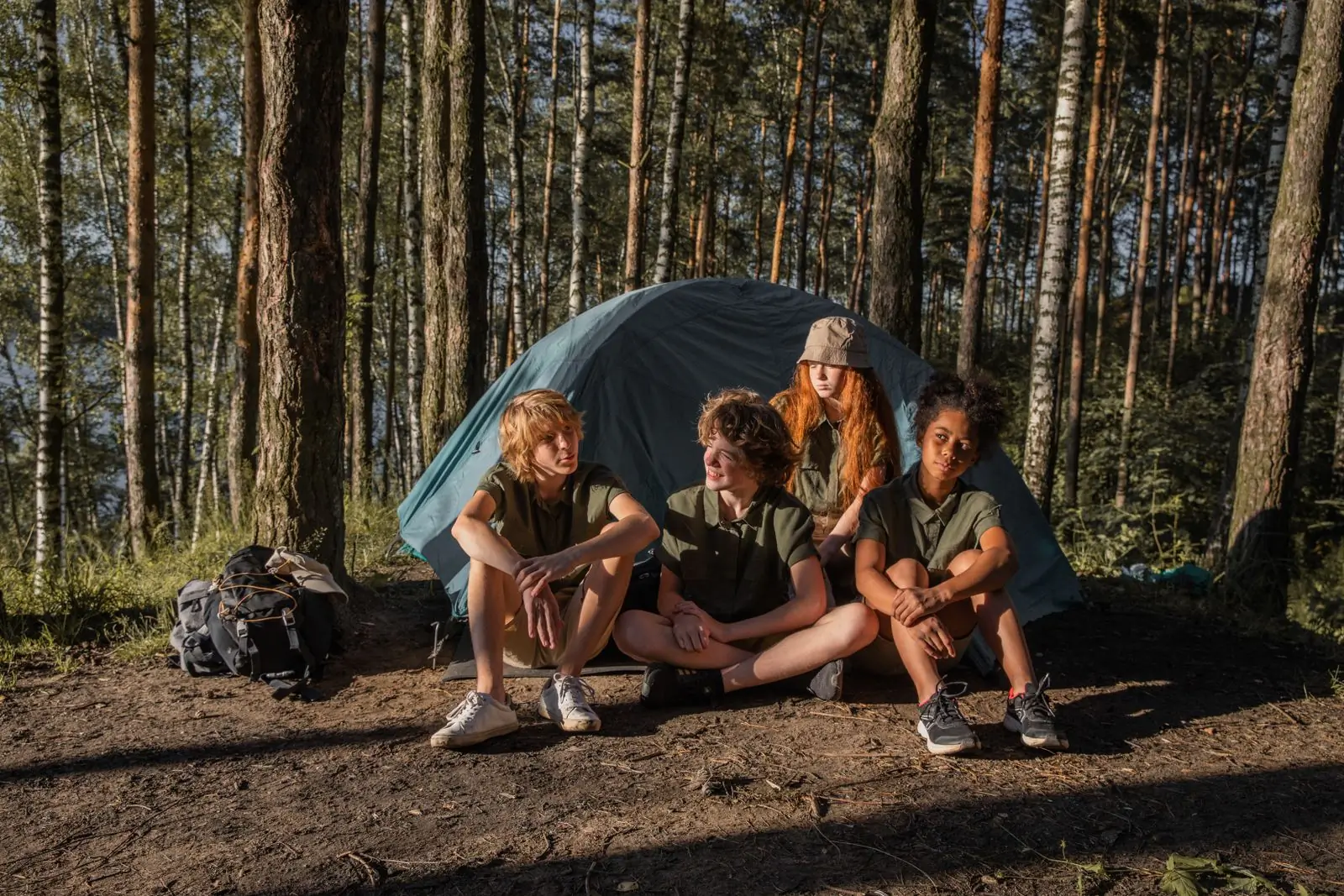 Campers sitting outside a tent in the pines at the end of the day