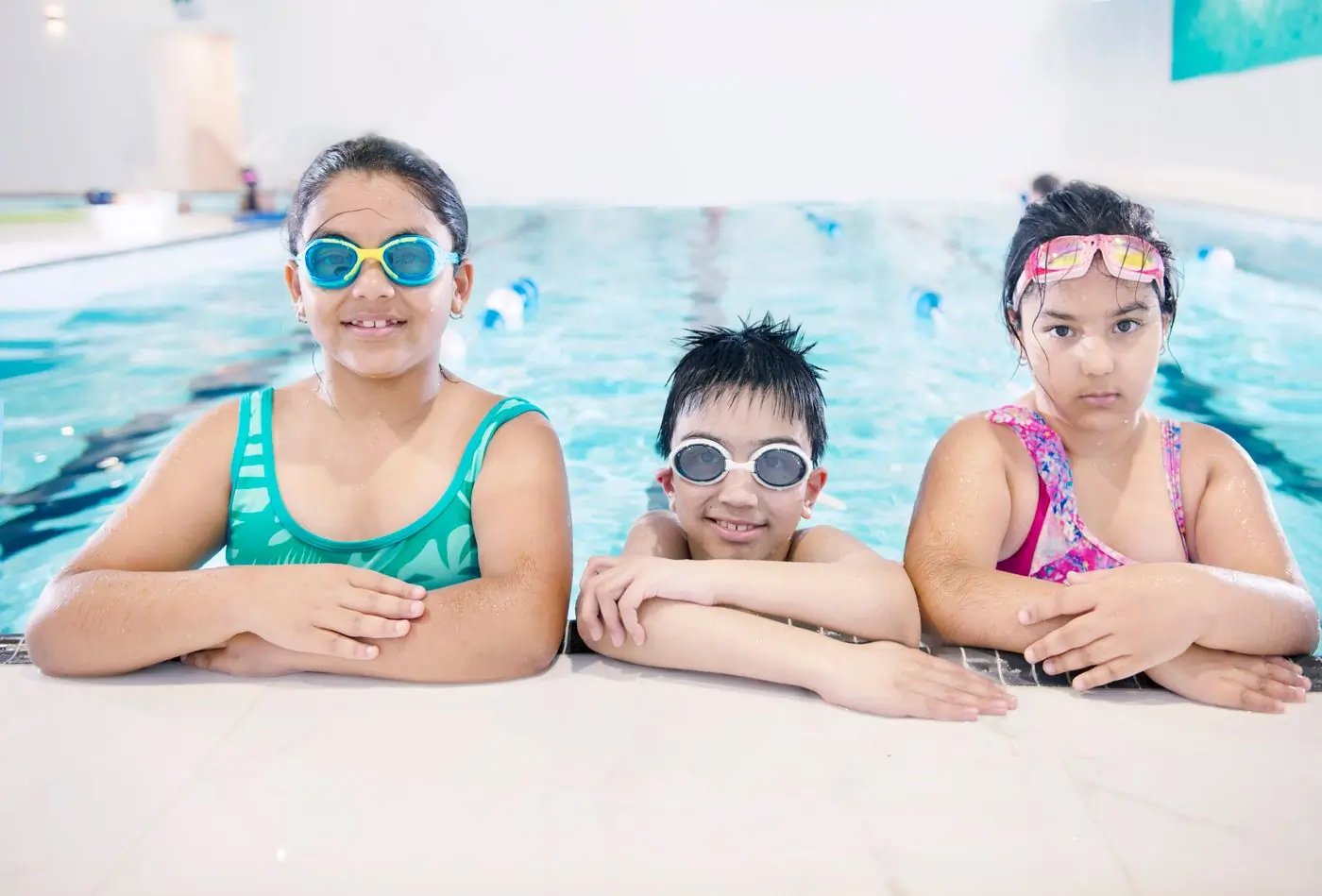 Three campers in goggles resting at the edge of the camp pool