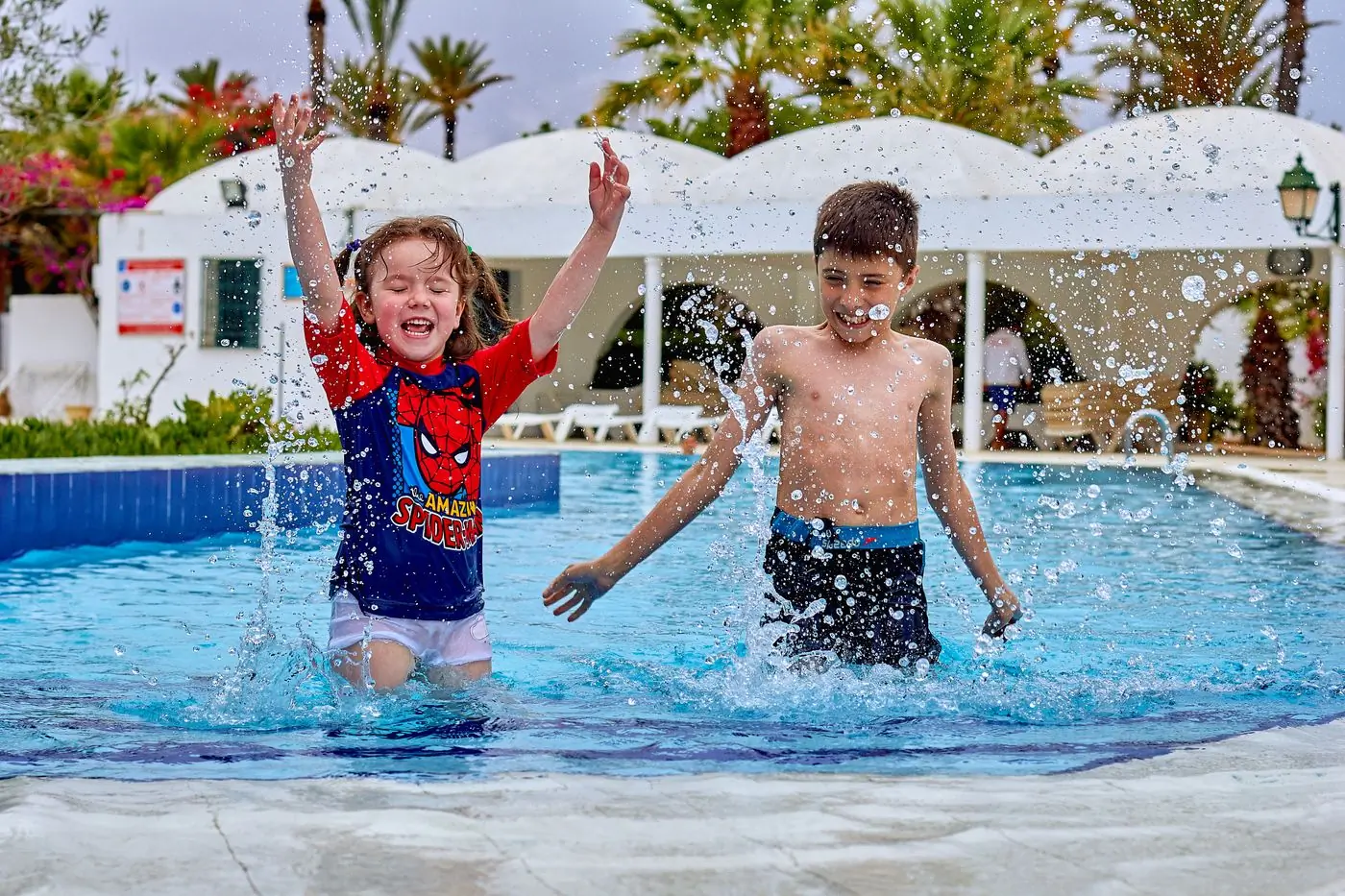 Two young campers leaping and splashing in the camp pool