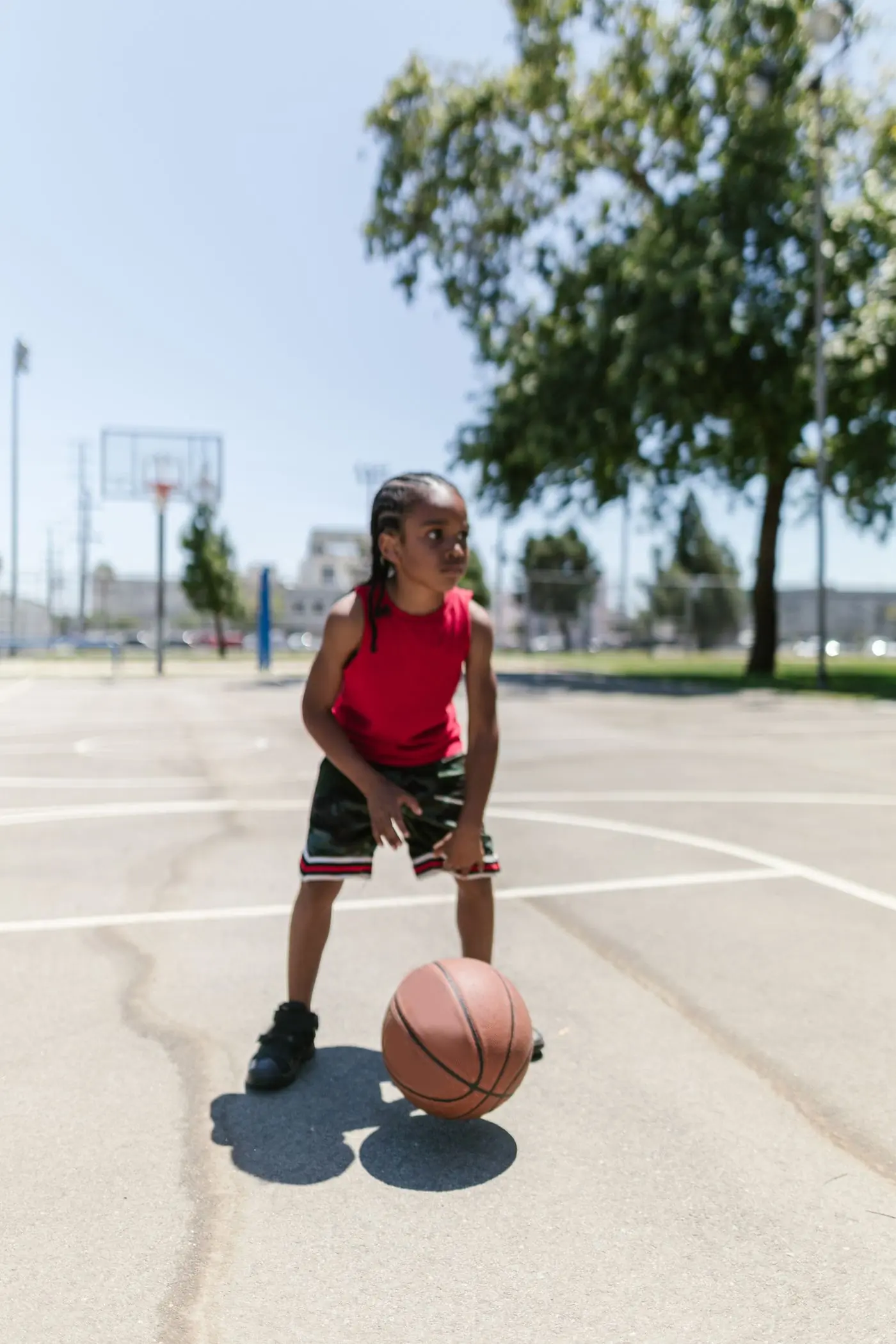 A camper in a red vest waiting on the ball at the outdoor basketball court