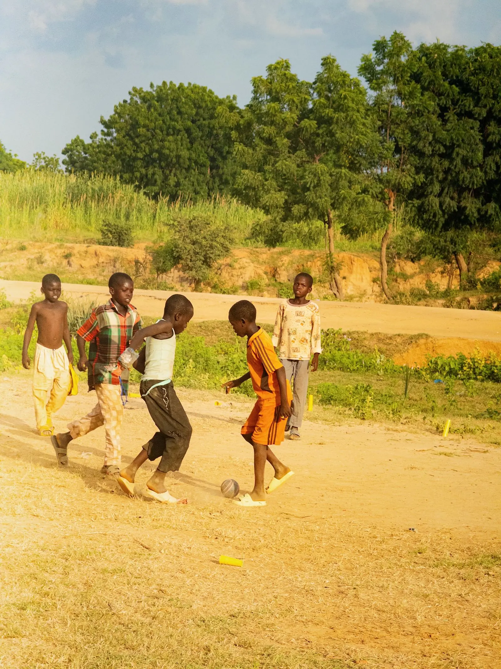 Children playing football on a dusty pitch in the late afternoon