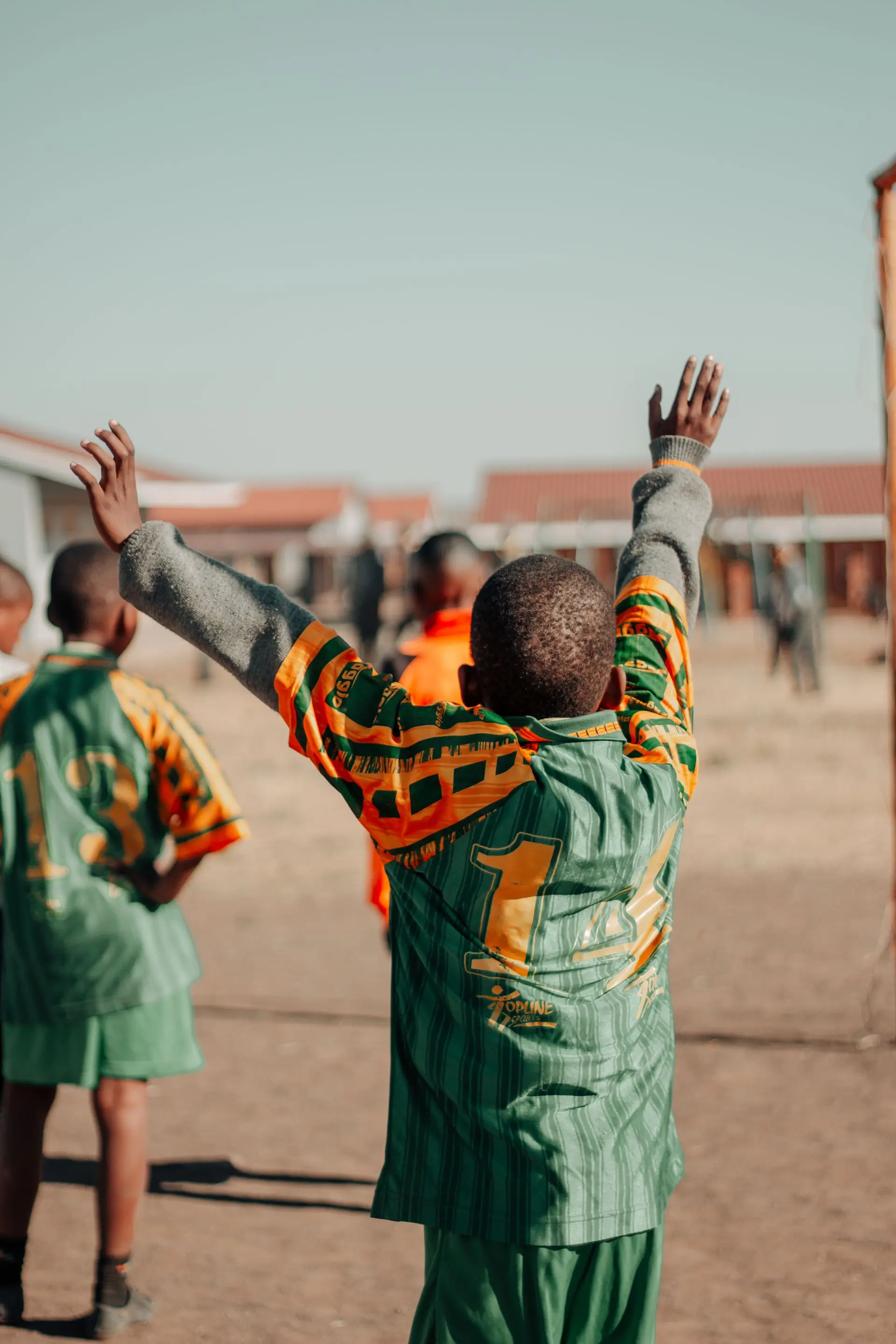 A camper in a green and gold kit raising both arms after a goal
