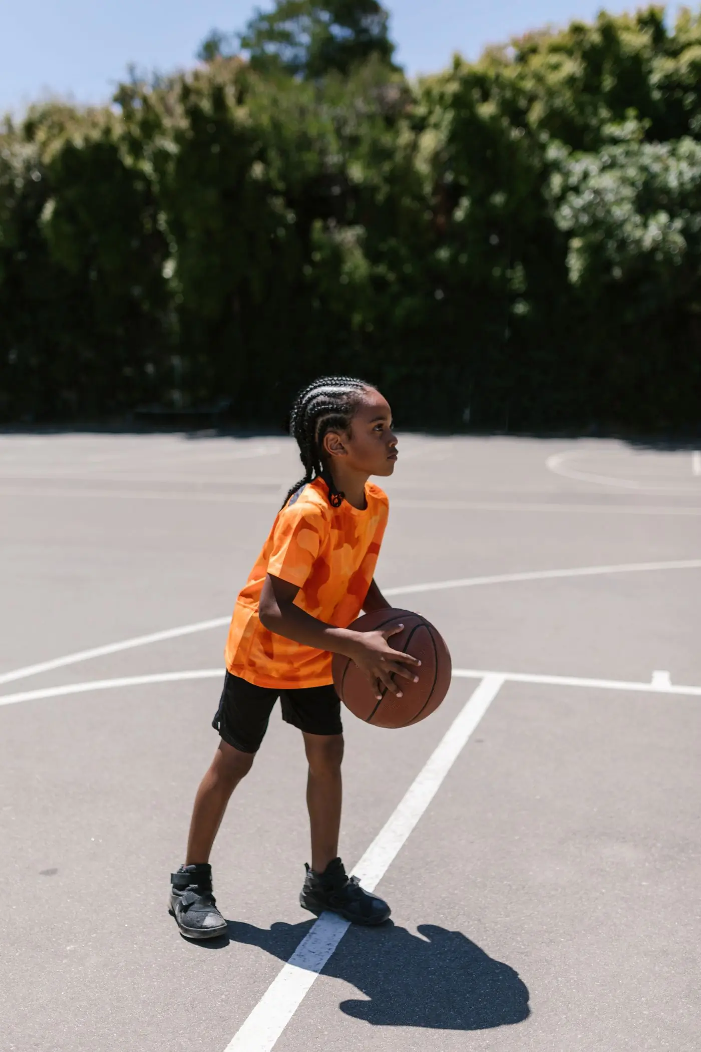 A camper in an orange training top setting up a shot on the basketball court