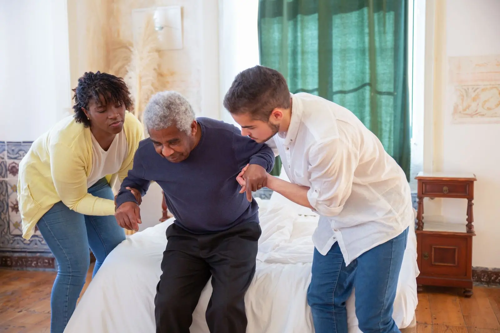 Two carers helping a patient to his feet at home