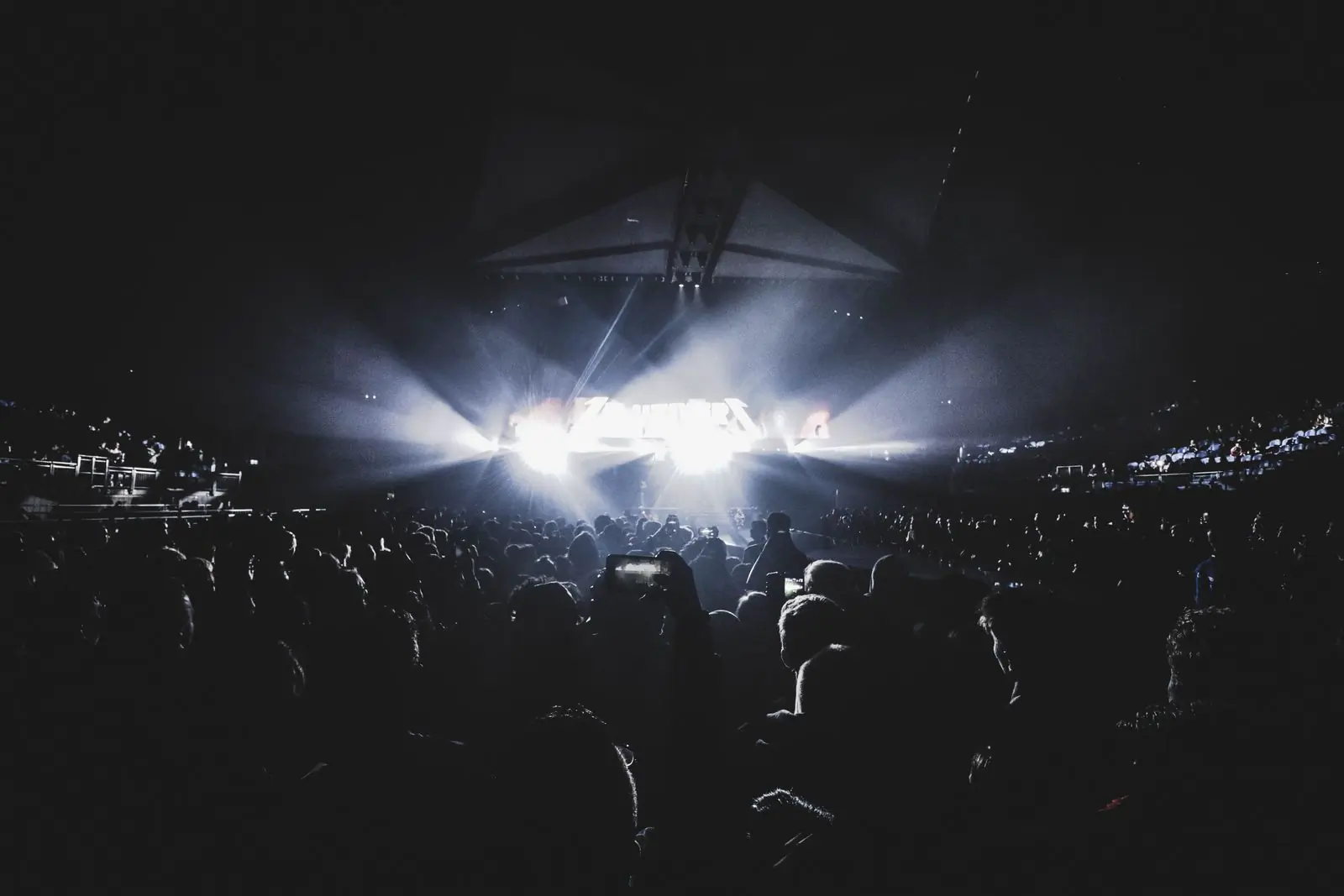 A packed arena with white beams cutting through the haze above the crowd