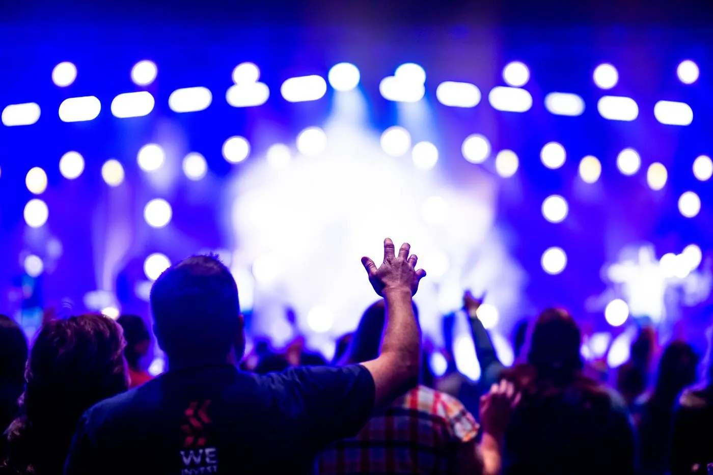A crowd in front of a wall of blue stage lights with hands raised