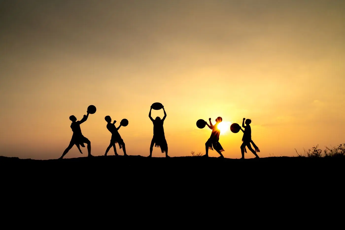 Drummers silhouetted against an orange sunset sky