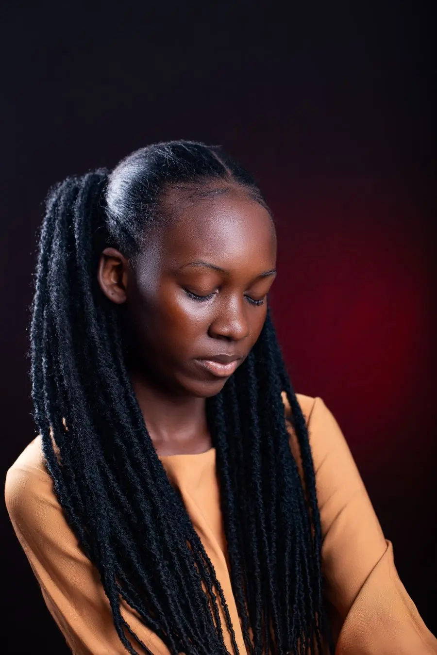 Adjoa Nyarko with locs, lit from one side against a deep red ground