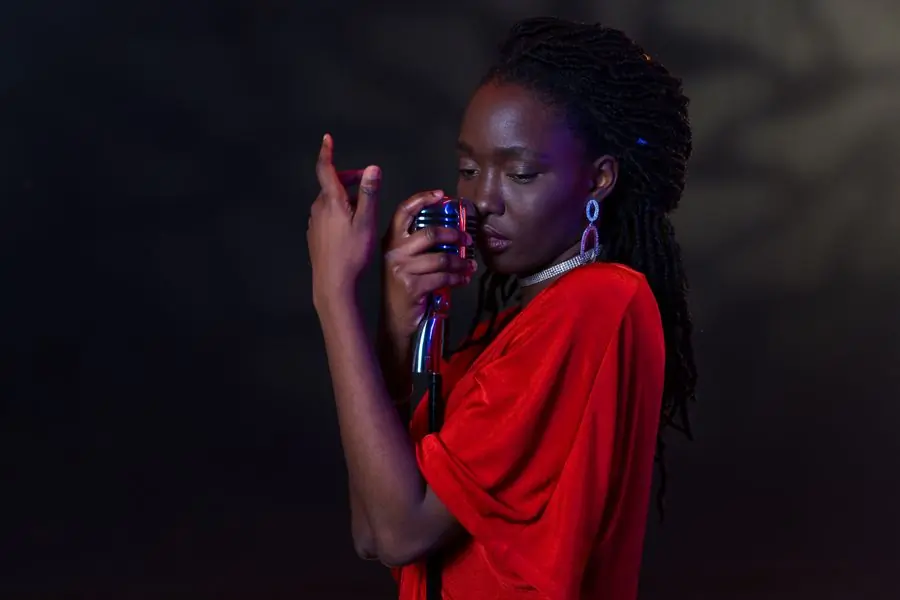 Efua Mensimah singing into a vintage microphone against a dark ground