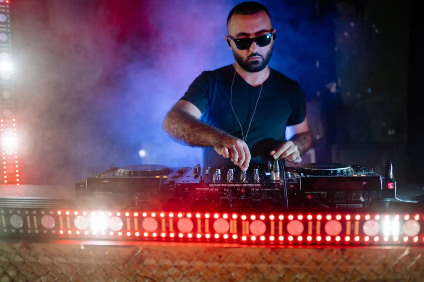 A DJ playing behind a red-lit booth in a smoky club