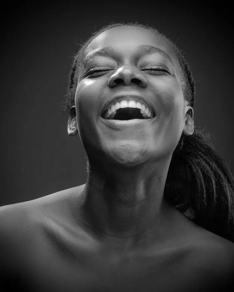 A woman laughing with her head tilted back, photographed in black and white