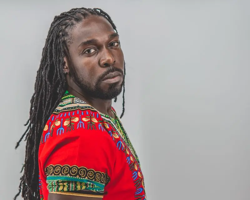 A man with locs in a brightly patterned shirt looking over his shoulder