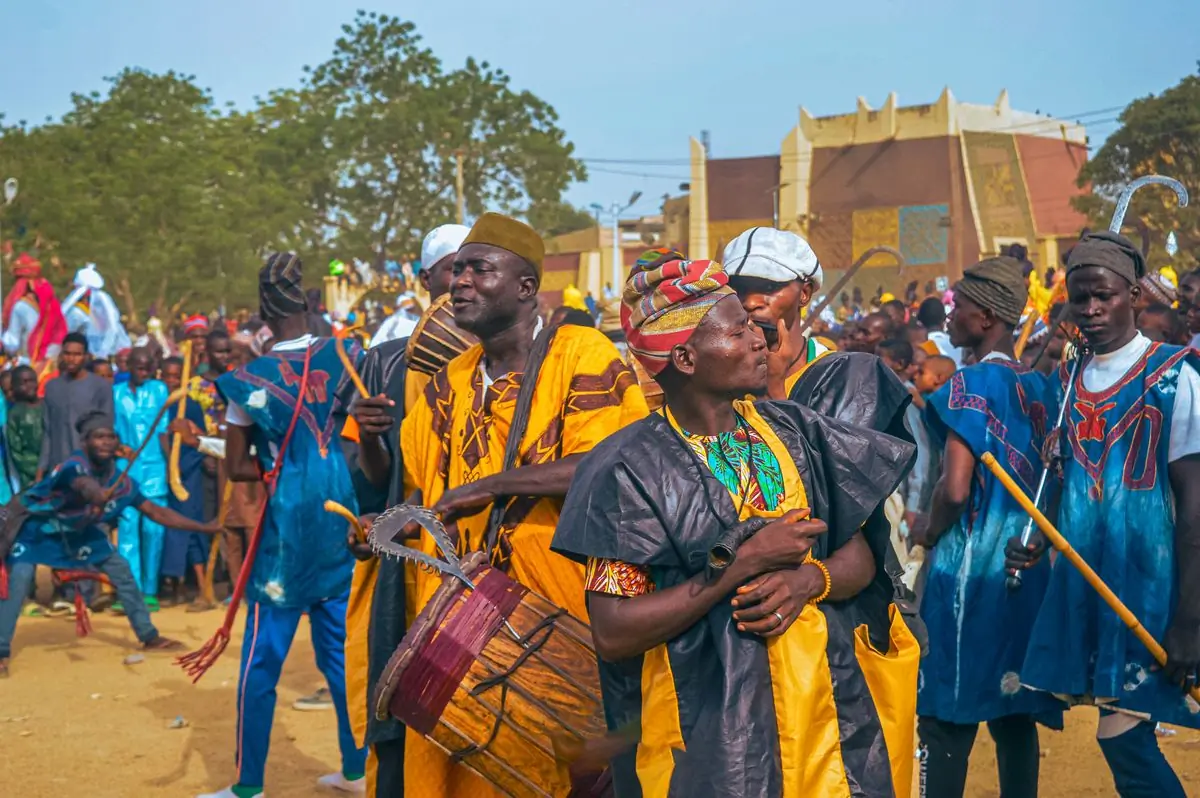 Drummers in yellow and blue robes playing in a crowd under a bright sky