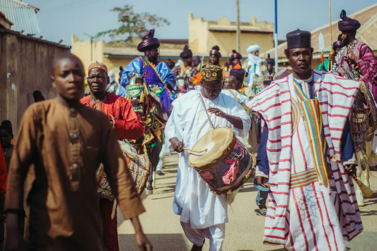 A drummer walking a sunlit street with a procession behind him