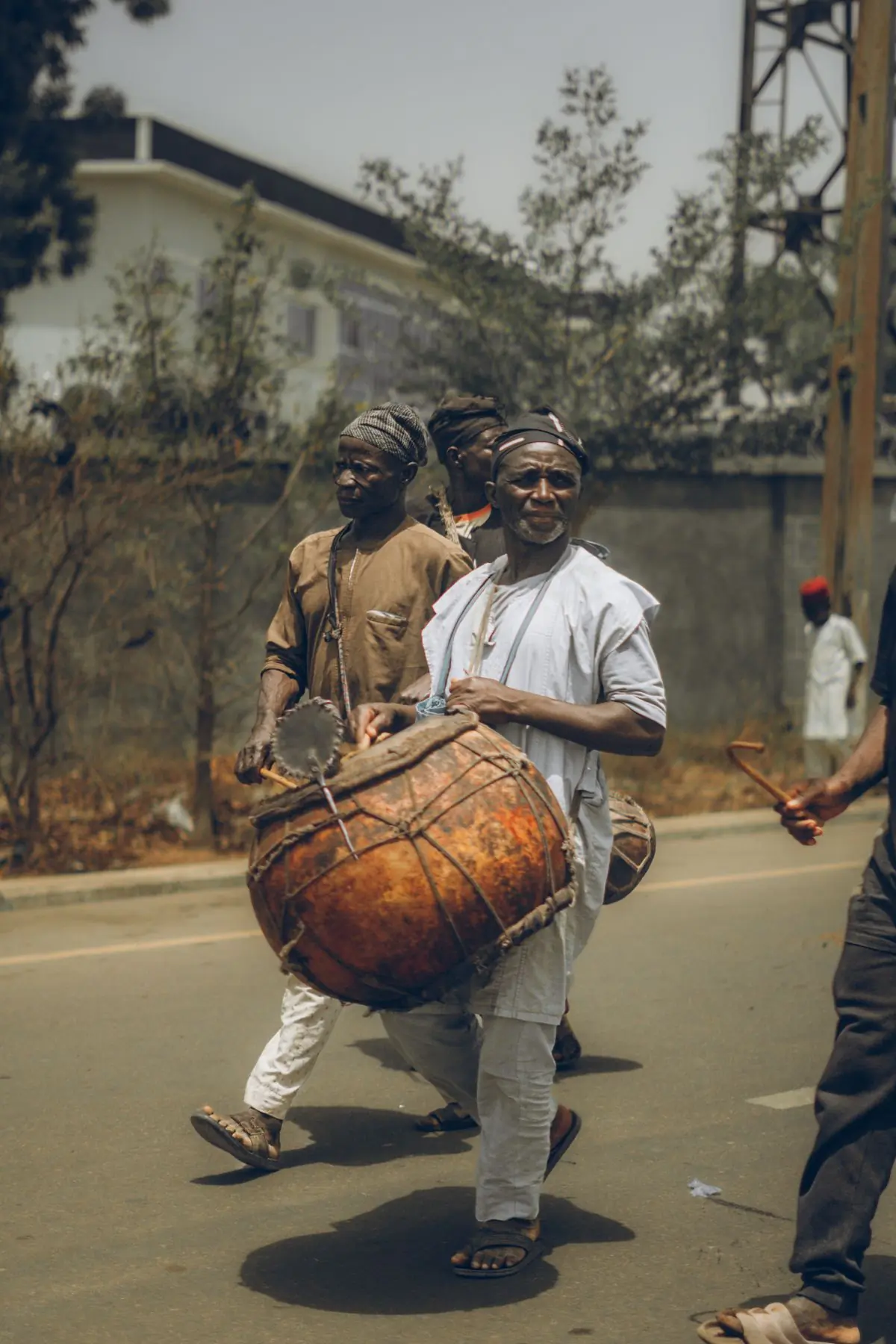 A procession of drummers walking a road carrying a large hand drum