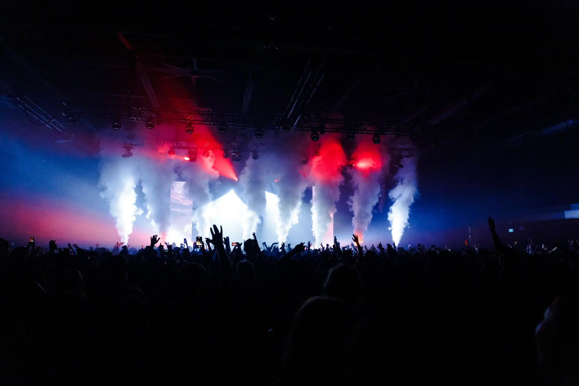 Jets of smoke and red light over a crowd at a night concert