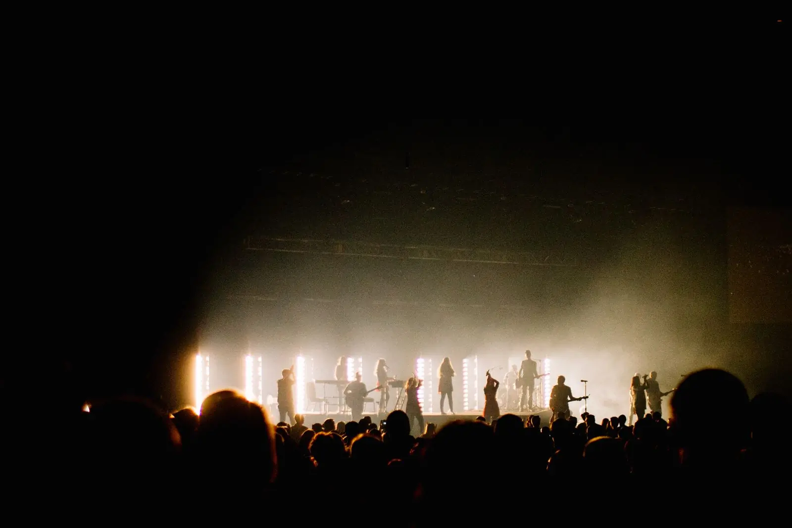 A band in silhouette on a warmly lit stage with the crowd's heads in the foreground