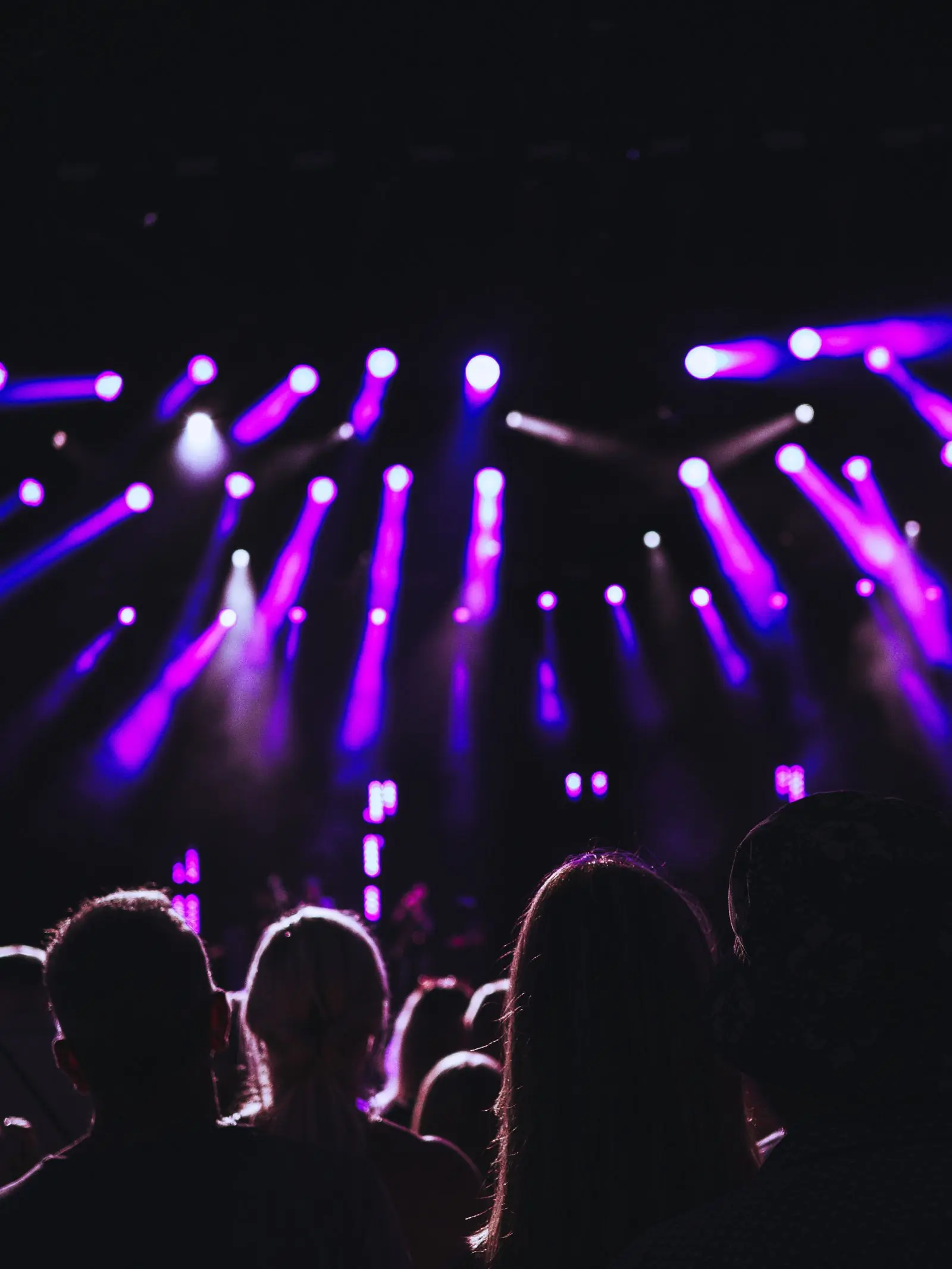Purple light beams sweeping over the heads of a night crowd