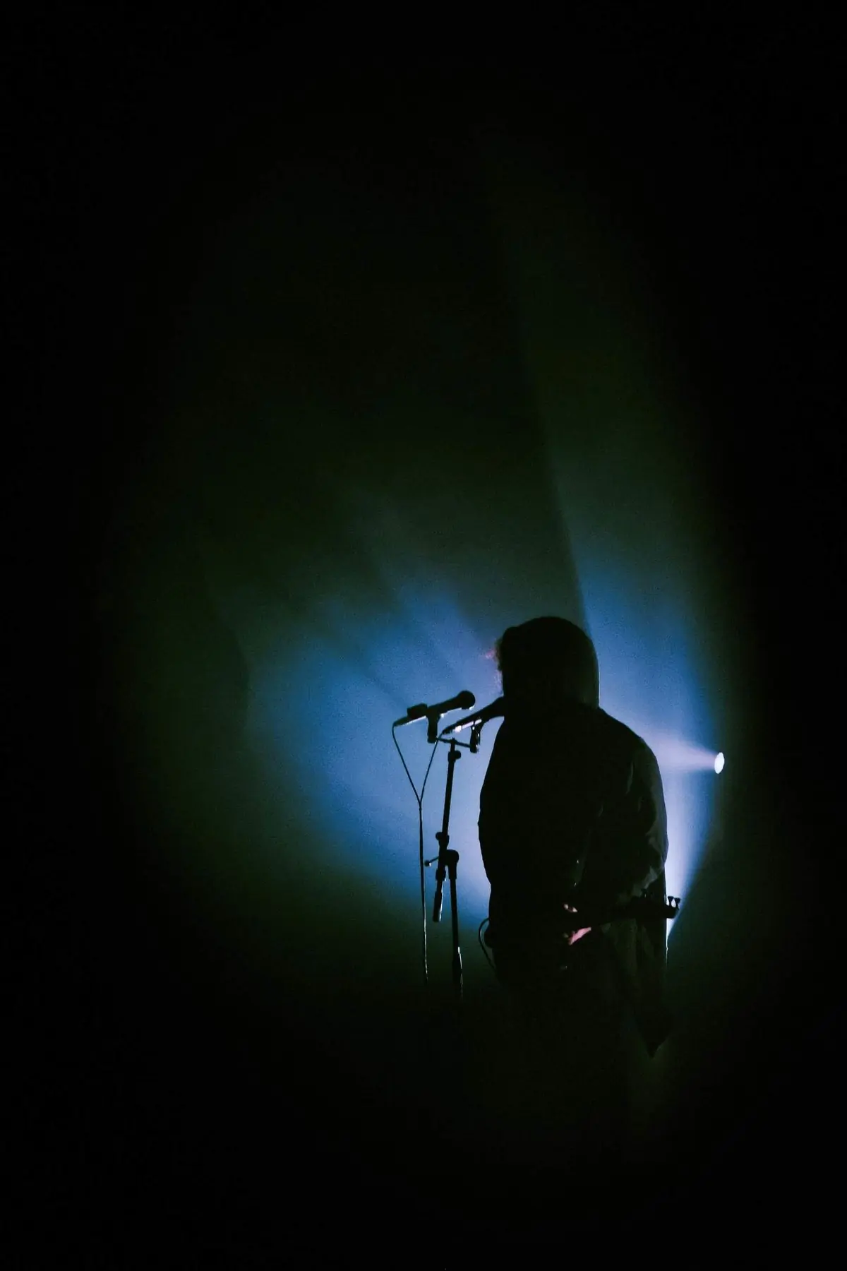 A singer in silhouette at a microphone against a wash of blue light