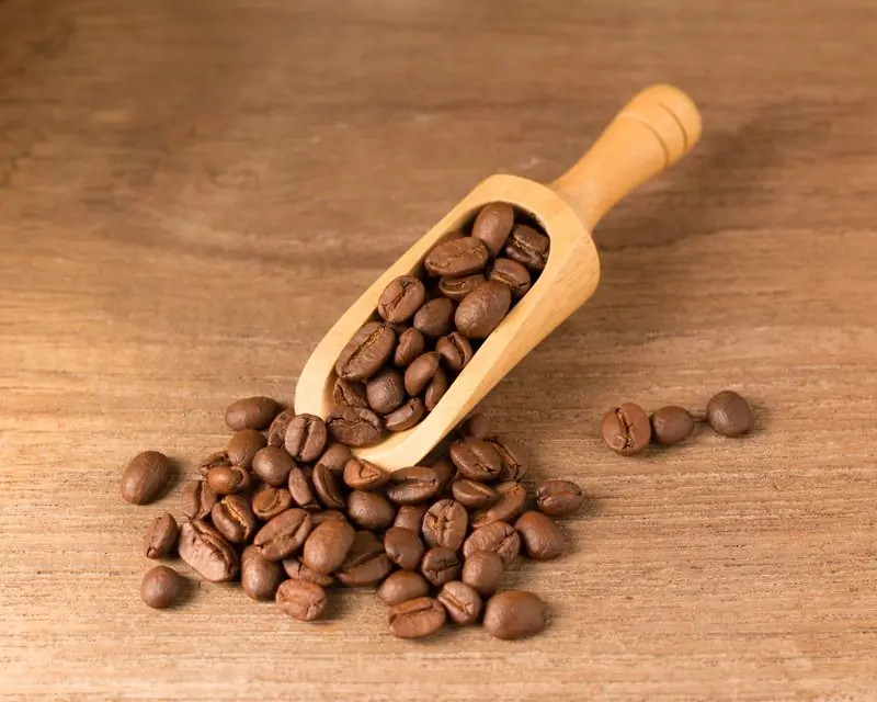 A wooden scoop of roasted beans tipped out across a honey-coloured table