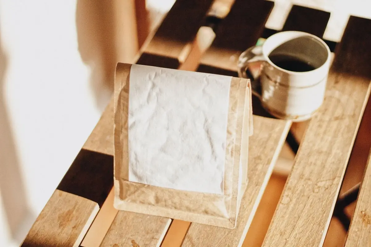 A kraft bag of the house blend on sunlit boards, beside a mug of black coffee