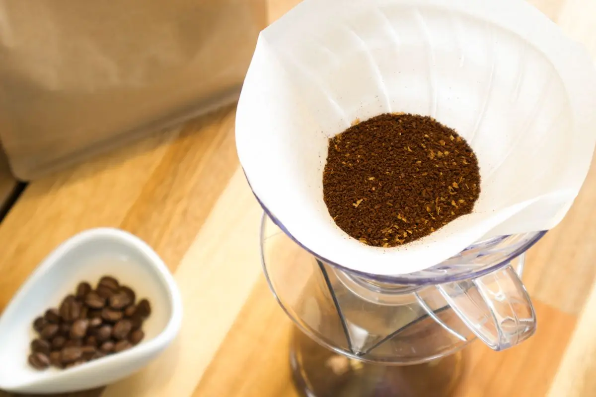 A single dose of ground coffee in a paper filter over a glass carafe