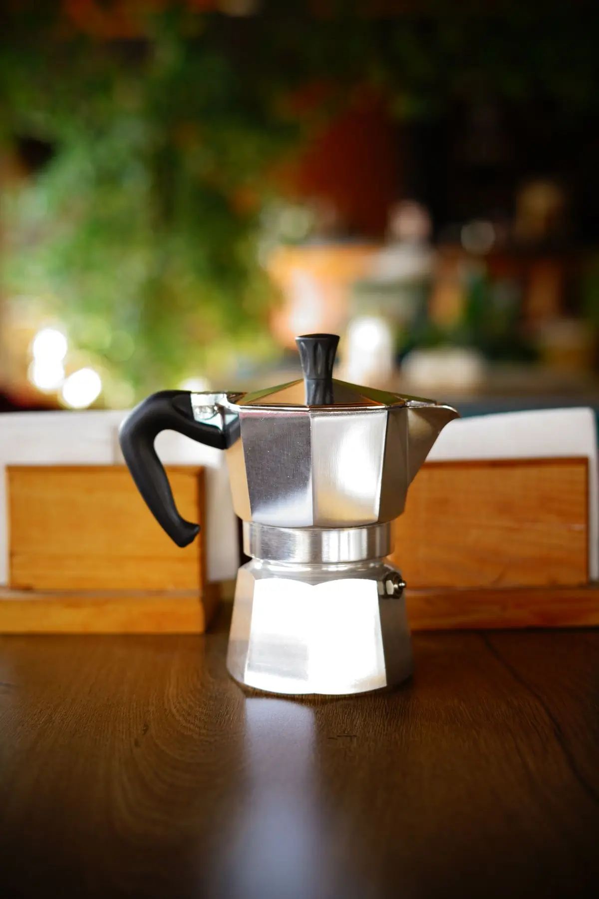 A polished stovetop espresso maker on a dark wooden table